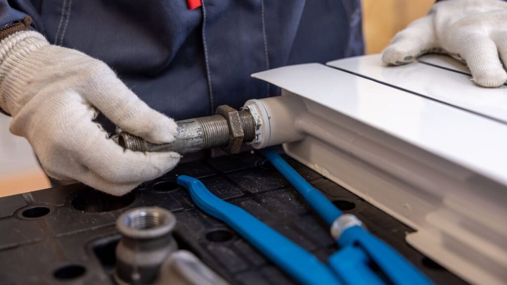 Monteur sluit leiding aan op radiator tijdens installatie van een modern verwarmingssysteem
