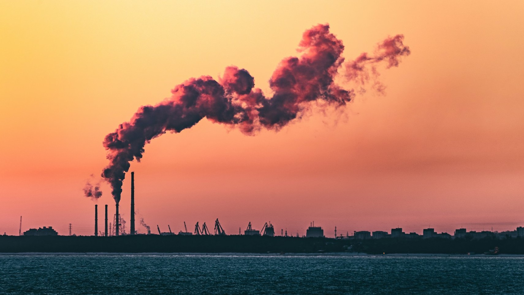 Rookpluimen uit fabrieksschoorstenen bij zonsondergang illustreren CO₂-impact op het milieu