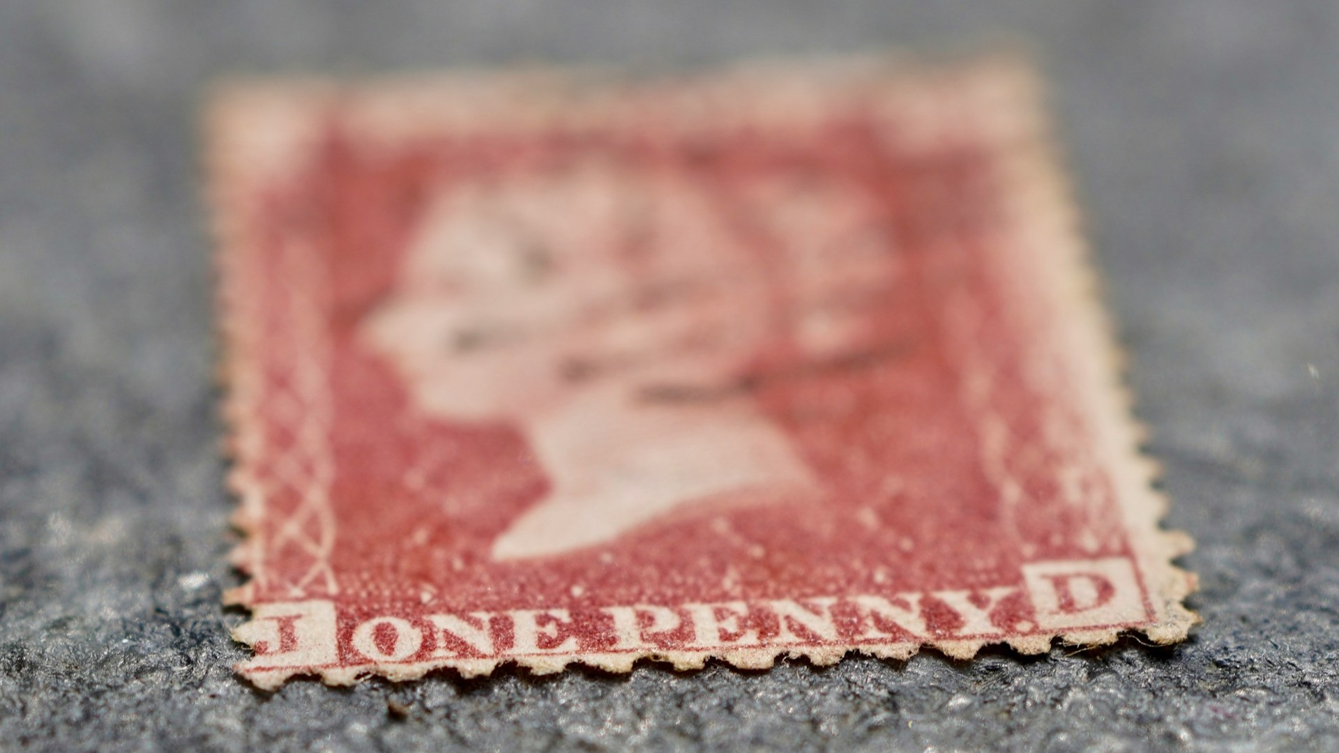 Vervaagde rode postzegel met zichtbare slijtage en kleurverlies, duidelijk voorbeeld van hoe postzegels vervagen door ouderdom en gebruik