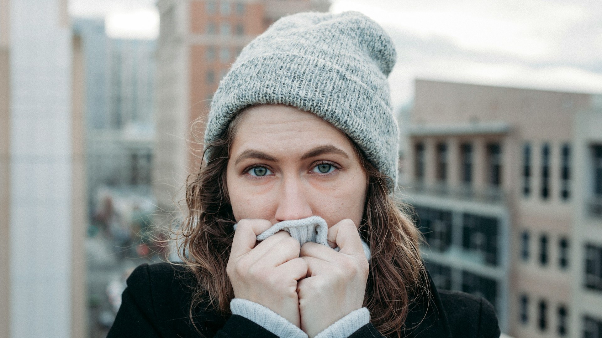 Vrouw met muts en koude handen voor gezicht toont hoe lichaamswarmte verliezen voelbaar wordt bij lage temperaturen