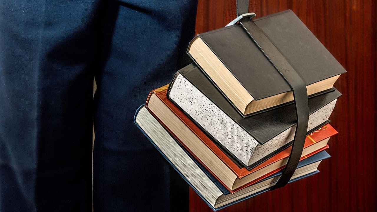 Stapel studieboeken vastgehouden door student als voorbereiding op het cursus kiezen en studietraject